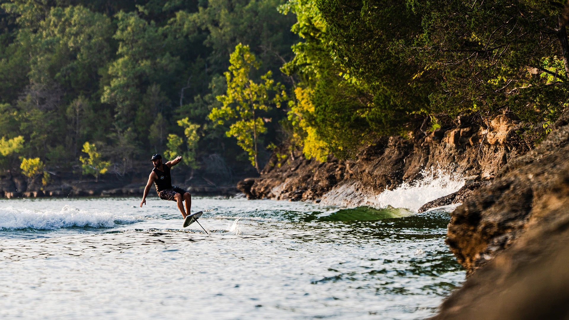 John Akerman riding the Phase Five Chopstick foil board beside a wooded shoreline