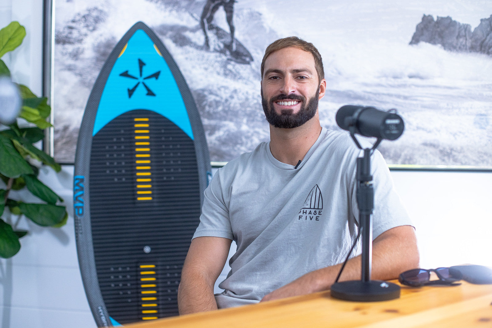 John Akerman smiling at the Phase Five podcast table with a wakesurf board behind him.